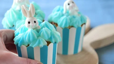Easter table setting.Hands place blue cupcakes with bunnies on a wooden board Stock Footage 299030732