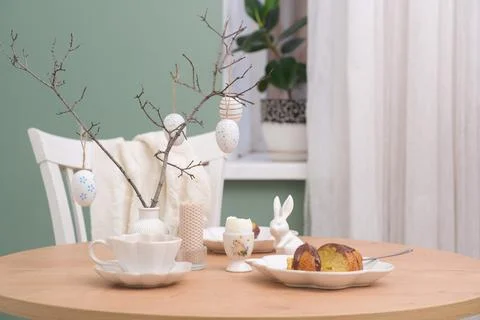Easter table. Vase with fresh branches, cup of tea, cupcake on plate, boiled egg Foto stock