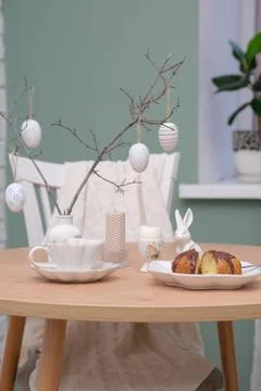 Easter table. Vase with fresh branches, cup of tea, cupcake on plate, boiled egg Stock-Fotos