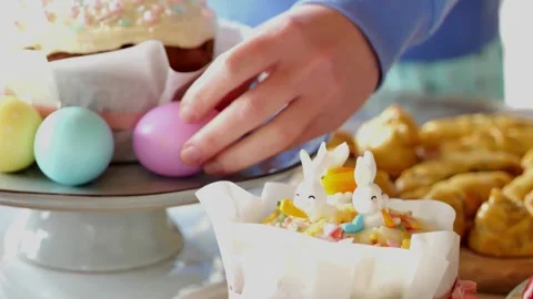 Easter table.Woman stacks painted eggs near Easter cake in bright room. Stock Footage 300289643