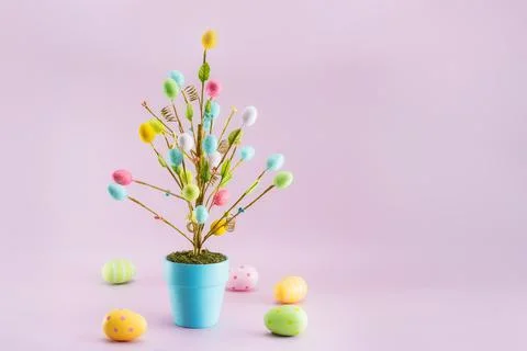 Easter tree decor in blue pot with colorful eggs around on the light pink Stock Photos
