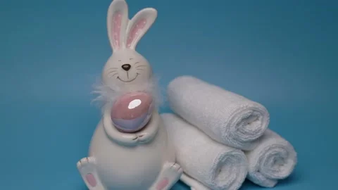 Easter white bunny wit brown egg blue background white towels Easter preparation Stock Footage 234110219