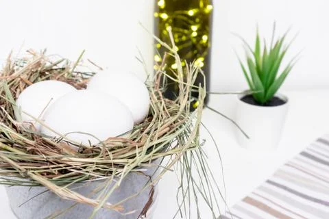 Easter white chicken eggs in straw nest, green spring plants and easter holid Stock Photos