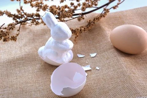 Easter white rabbit and the shell of a broken egg on a beige tablecloth and.. Stock Photos