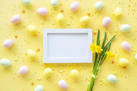 Easter yellow eggs with white frame and flowers on a yellow background. Stock Photos