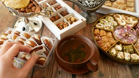 Eastern sweets with nuts, candy, metal vase, tea, dates on wooden background, Stock Footage 147984805