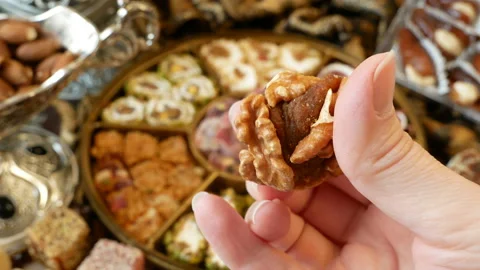 Eastern sweets with nuts, candy, metal vase, tea, dates on wooden background, Video stock 147985322