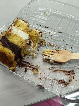 Eaten slice of cake in plastic container. Reusable wooden fork for take out food Stock Photos