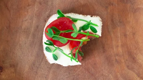 Eating bite by bite small toast with cream cheese, tomatoes and pea sprouts. Stock Footage 129173996