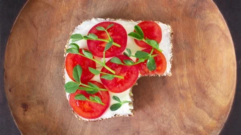 Eating bite by bite a toast with cream cheese, tomatoes and pea sprouts. Stock Footage 129174114
