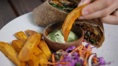 Eating clean concept. Hand dipping sweet potato in green creamy sauce. Vegan Video stock 146056473