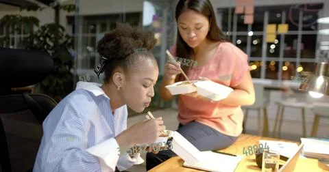 Eating lunch two colleagues using chopsticks at desk in office workspace, with Stock Photos
