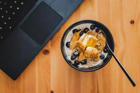 Eating mango blueberries oatmeal while working from home on a laptop, remote  Stock Photos