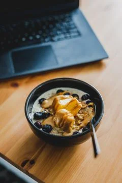 Eating mango blueberries oatmeal while working from home on a laptop, remote  Stock Photos