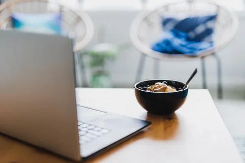 Eating mango blueberries oatmeal while working from home on a laptop, remote  Stock Photos