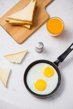 Eating in the process, fried eggs in a frying pan, toast  and orange juice fo Foto stock