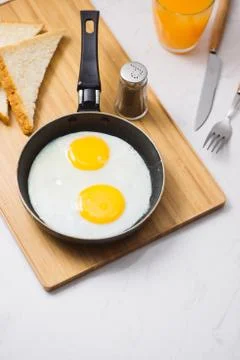 Eating in the process, fried eggs in a frying pan, toast  and orange juice fo Stock Photos