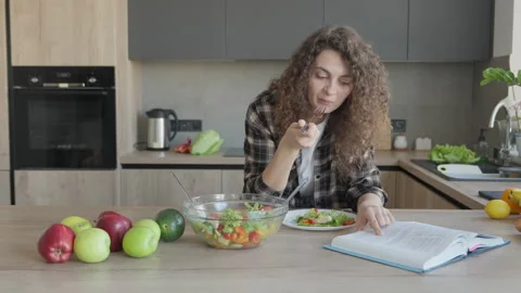 Eating Salad While Reading Cookbook In Bright Modern Kitchen Scene 動画素材 311271380