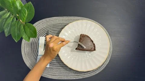 Eating slice of chocolate cake with fork from white plate, top view flat lay Stock-Fotos