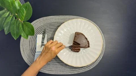Eating slice of chocolate cake with fork from white plate, top view flat lay Stock-Fotos