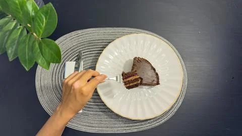 Eating slice of chocolate cake with fork from white plate, top view flat lay Stock-Fotos
