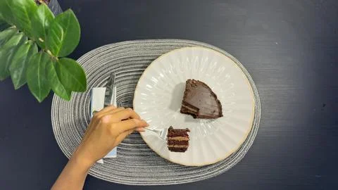 Eating slice of chocolate cake with fork from white plate, top view flat lay Stock Photos