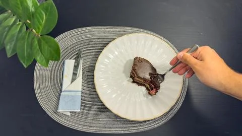 Eating slice of chocolate cake with fork from white plate, top view flat lay Stock Photos