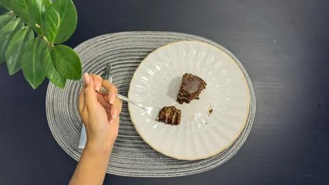 Eating slice of chocolate cake with fork from white plate, top view flat lay Stock-Fotos