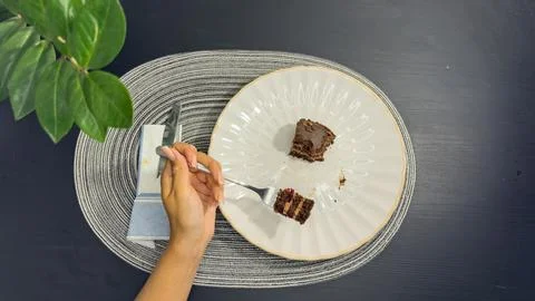 Eating slice of chocolate cake with fork from white plate, top view flat lay Stock Photos