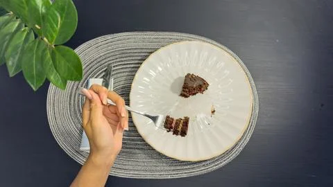 Eating slice of chocolate cake with fork from white plate, top view flat lay Stock Photos