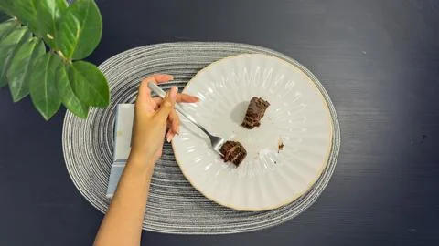 Eating slice of chocolate cake with fork from white plate, top view flat lay Stock Photos