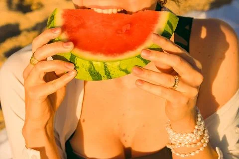 Eating watermelon on beach during sunset with hands holding  slice and wearin Stock Photos