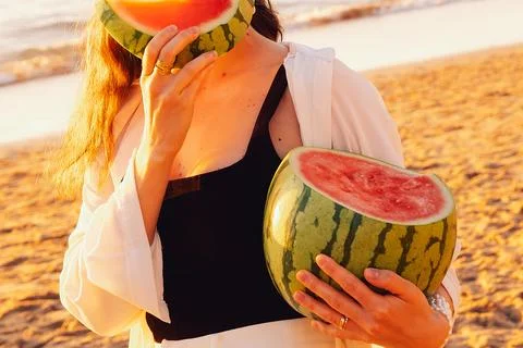 Eating watermelon on beach during sunset with hands holding  slice and wearin Stock Photos