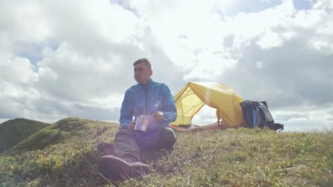 Eating while hiking in the mountains, a man sits near a tent on a sunny day Stock Footage 218441204