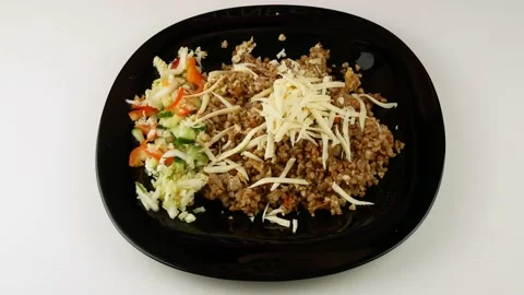 Eats lunch with a fork.Buckwheat with vegetables on a black plate. Stock Footage 140804909