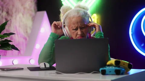 Eccentric grandma in a headset playing on a laptop, upset after losing the game Stock Footage 333682199