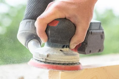 An eccentric sander in the hands of a worker grinds a wooden surface, close-up Stock Photos