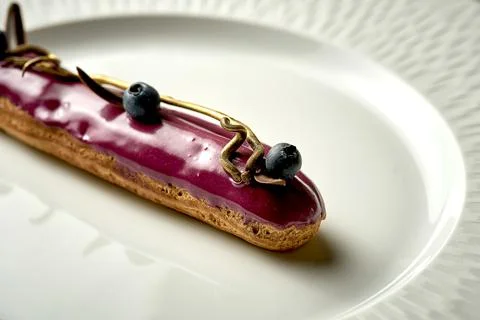 Eclair with berry glaze on a plate. Noise added in post-production. Selective Stock Photos