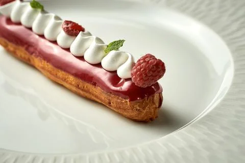 Eclair with berry glaze on a plate. Noise added in post-production. Selective Stock Photos