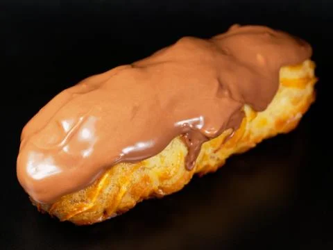 Eclair with chocolate icing. One eclair against a dark background. Stock Photos