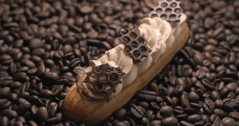 Eclair with coffee cream and chocolate pieces lies on the coffee beans Stock Footage 143782989