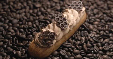 Eclair with coffee cream and chocolate pieces lies on the coffee beans Video stock 143782993
