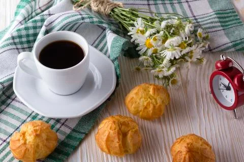 Eclair, coffee cup, alarm clock and charmomile. Stock Photos