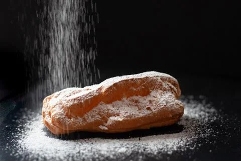 Eclair with cream on a black background. Sprinkle eclair with powdered sugar. Stock Photos