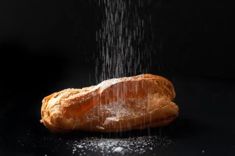 Eclair with cream on a black background. Sprinkle eclair with powdered sugar. Stock Photos