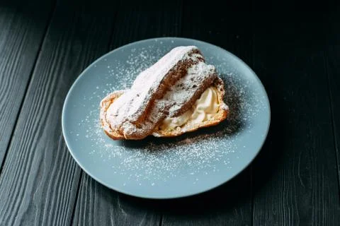 Eclair with cream is divided in half. Eclair on a plate on a black background Stock Photos