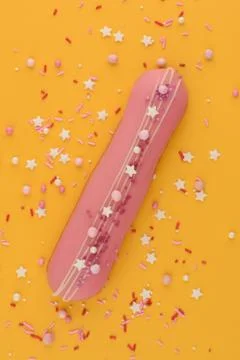 Eclair with decorative sweet sprinkles on a yellow background. Stock Photos