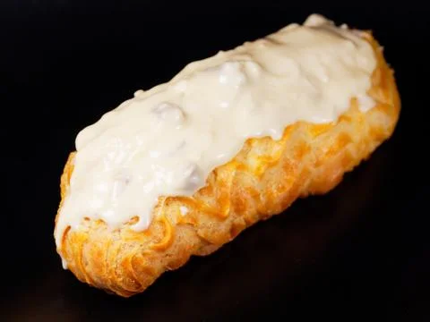 Eclair with white chocolate icing. One eclair against a dark background. Stock Photos