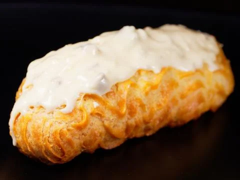 Eclair with white chocolate icing. One eclair against a dark background. Stock Photos