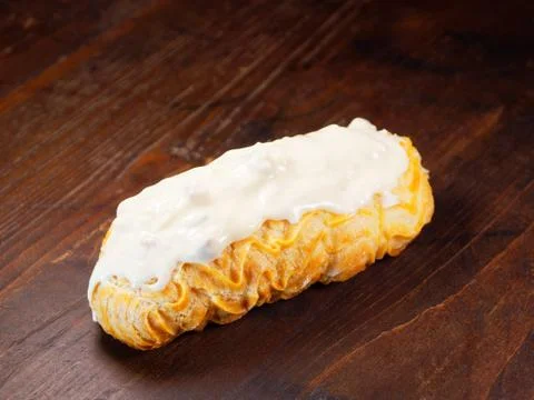 Eclair with white chocolate icing. One eclair on a wooden vintage background. Stock Photos